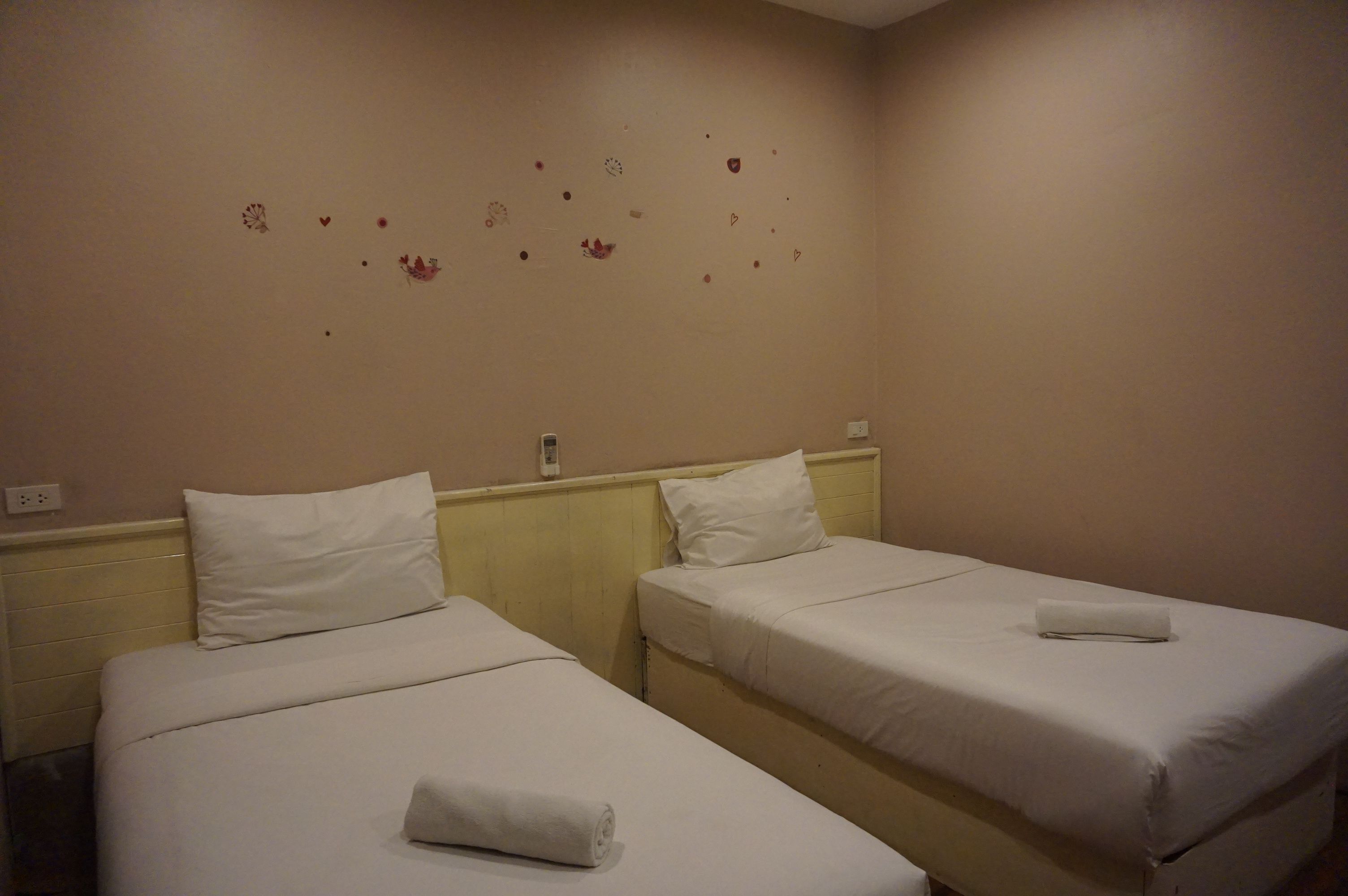 A hotel room with two single beds, each with a white mattress and pillow, and a small bedside table.