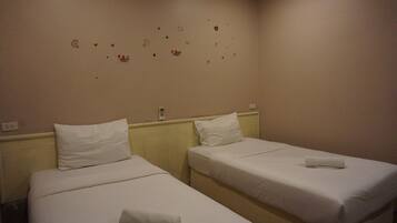 A hotel room with two single beds, each with a white mattress and pillow, and a small bedside table.