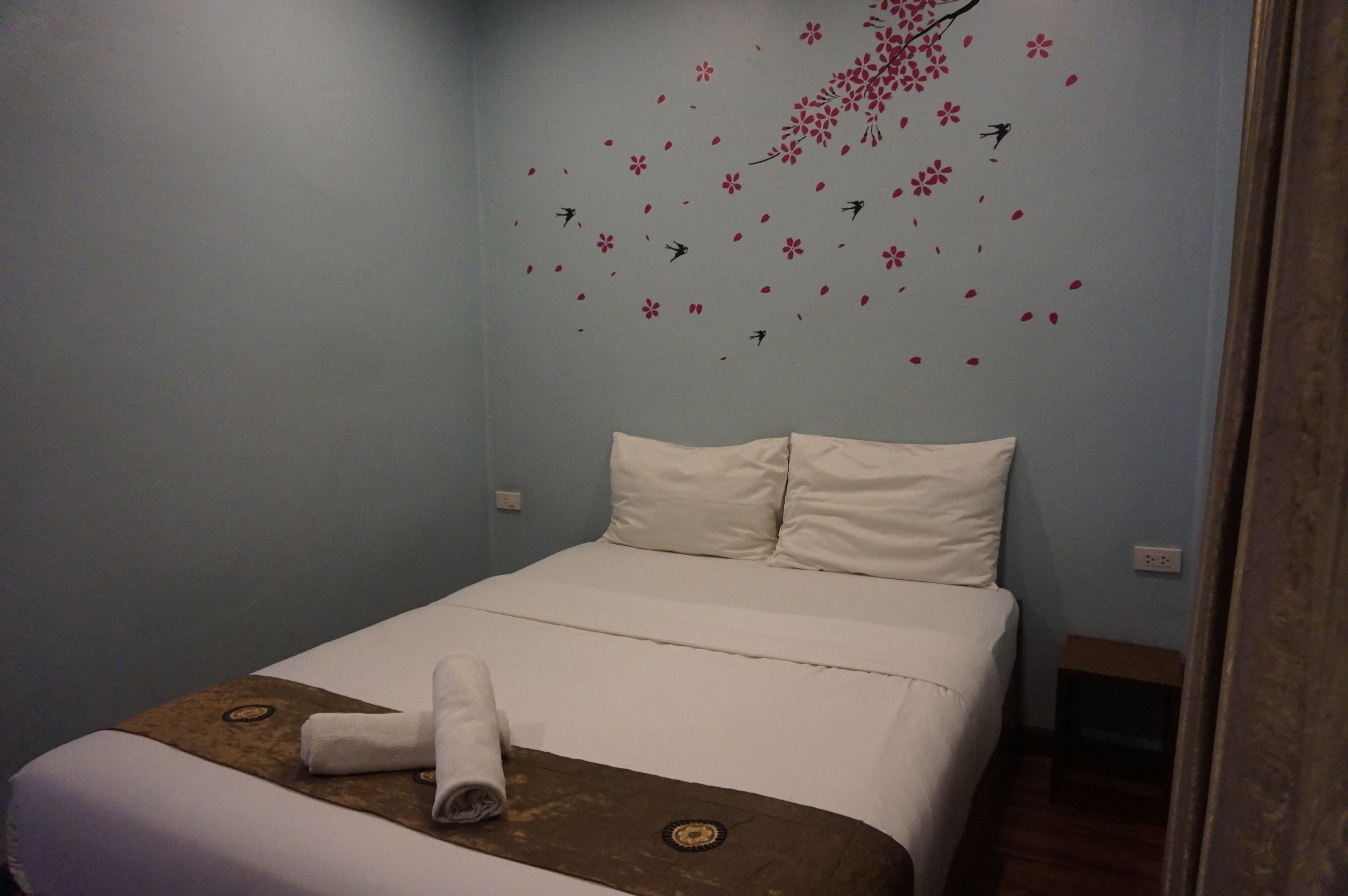 A hotel room with a bed, pillows, a rolled towel, and a wall with a cherry blossom design.