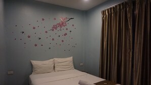 A hotel room with a bed, white bedding, a brown headboard, a window with curtains, and a wall decoration of birds and flowers. - Queens Hotel (Chum Phae)