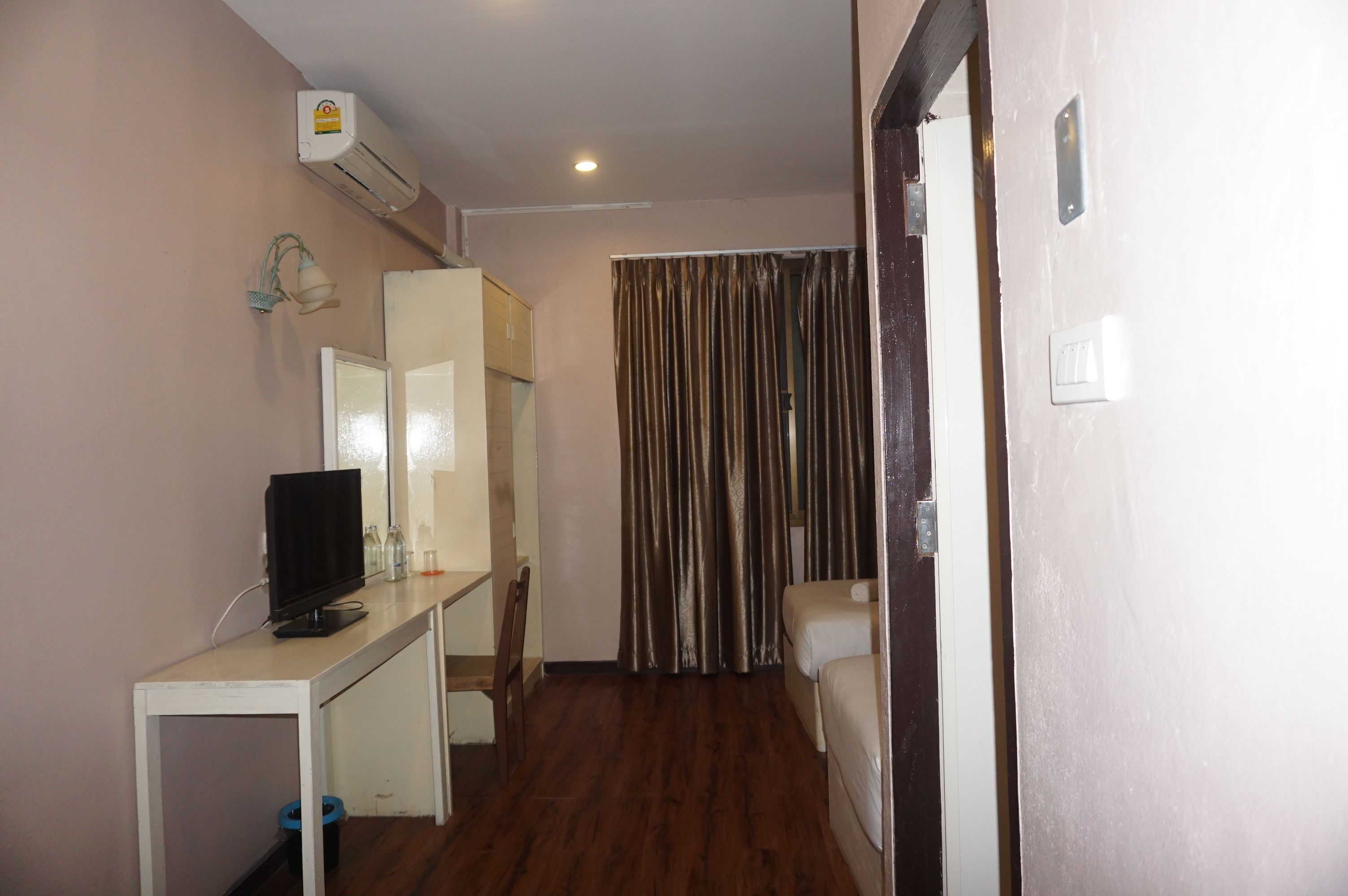 A small room with a desk, a chair, a bed, a curtain, and an air conditioning unit.