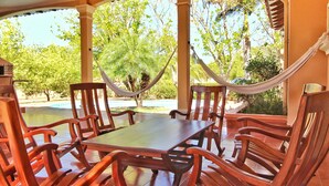 A covered patio with wooden furniture, a hammock, and a view of trees and a pool. - Casa Dror Gran Pacifica Resort (Villa El Carmen)