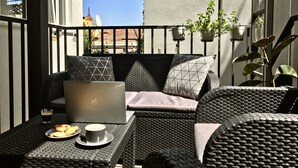 Een balkon met rieten meubels, een laptop, een kop koffie en een bord koekjes.
