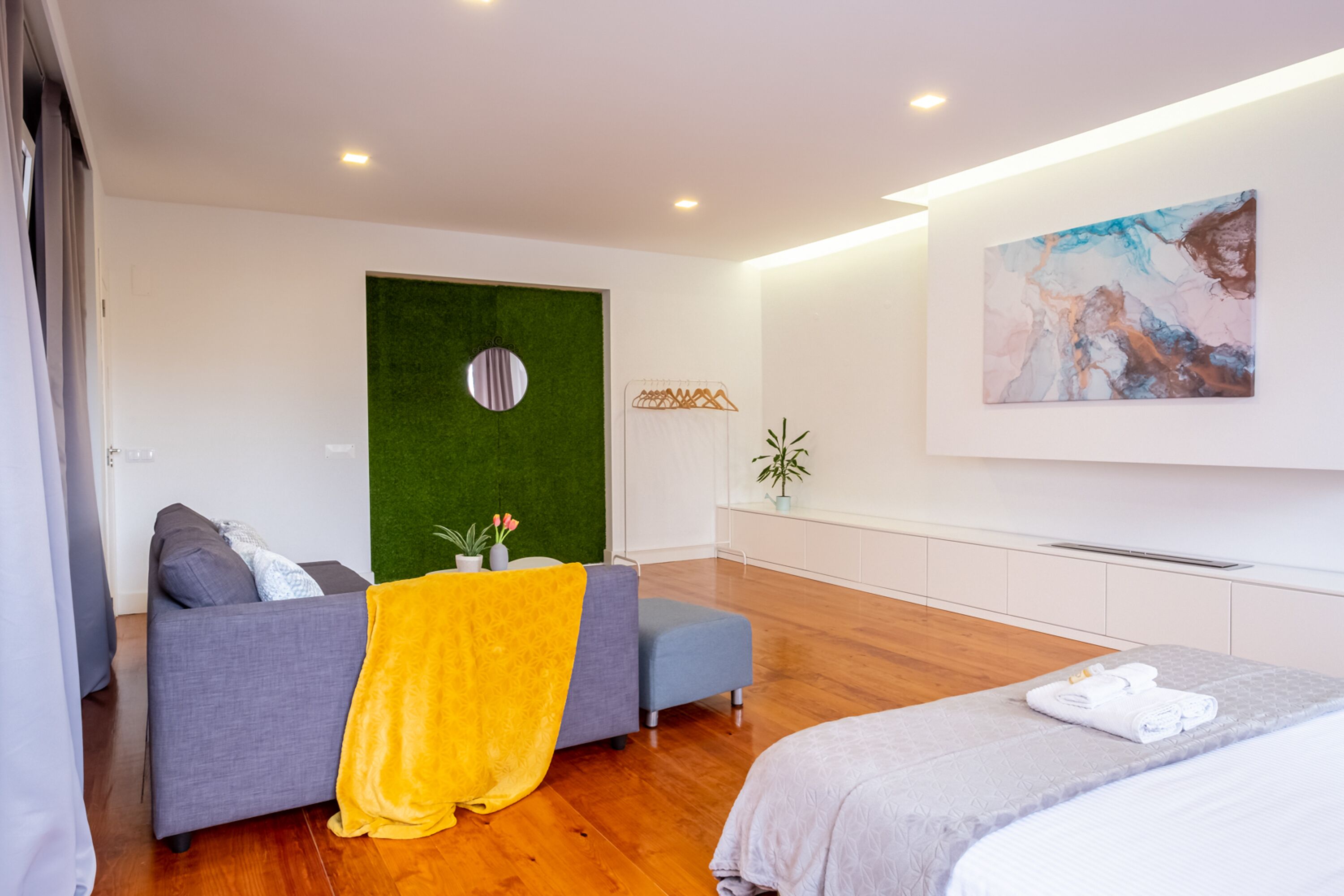 Ett modernt hotellrum med en grå soffa, en gul pläd, en grå säng och en grön accentvägg.