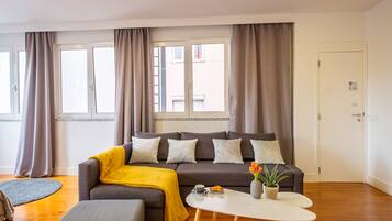 A modern living room with a grey sofa, a yellow throw blanket, a white coffee table, and a potted plant.