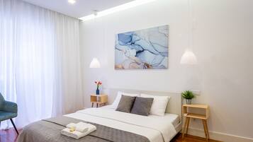 Ein modernes Schlafzimmer mit einem großen Bett, weißen Vorhängen, einem Bild an der Wand und zwei Nachttischen.
