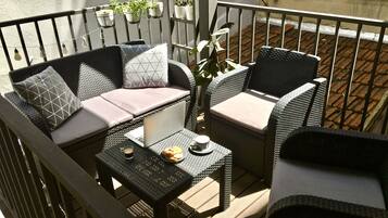 A balcony with wicker furniture, including a sofa and chairs, a small table with a laptop, and potted plants.