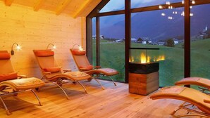 A cozy room with wooden floors, a fireplace, and large windows offering a view of the outdoors. - Erlebnishotel Gassenhof (Racines)
