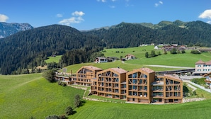 A large wooden building with multiple floors and balconies, surrounded by green fields and mountains. - Erlebnishotel Gassenhof (Racines)