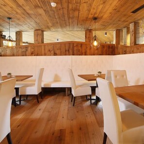 A restaurant with wooden panel walls, white cushioned seating, and hanging pendant lights. - Erlebnishotel Gassenhof (Racines)