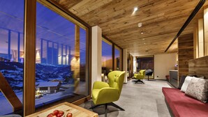 A modern interior with large windows, a wooden ceiling, and a cozy seating area with a red sofa and green chairs. - Erlebnishotel Gassenhof (Racines)
