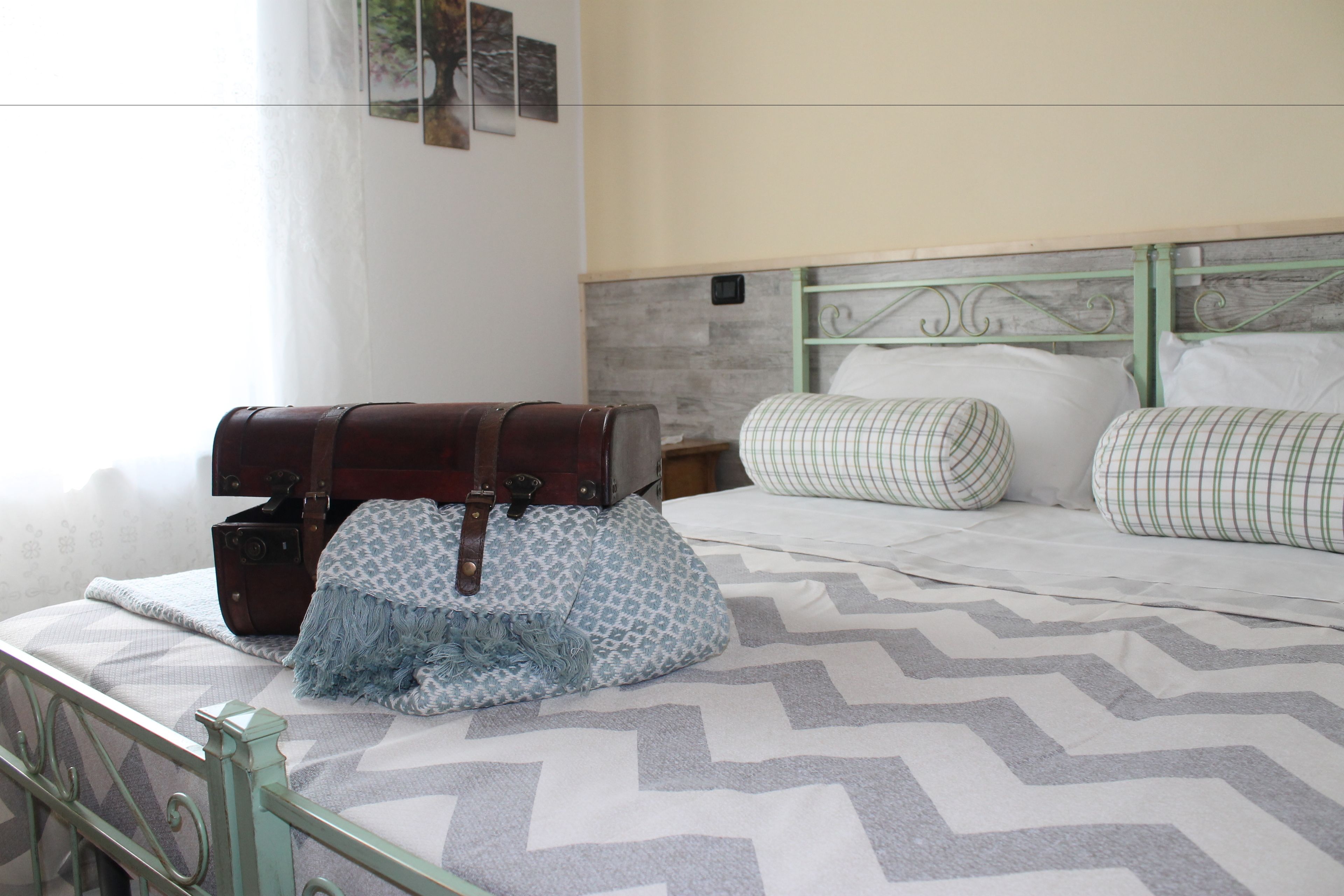 A bed with a chevron-patterned bedspread, a suitcase, and a patterned bag on the side.