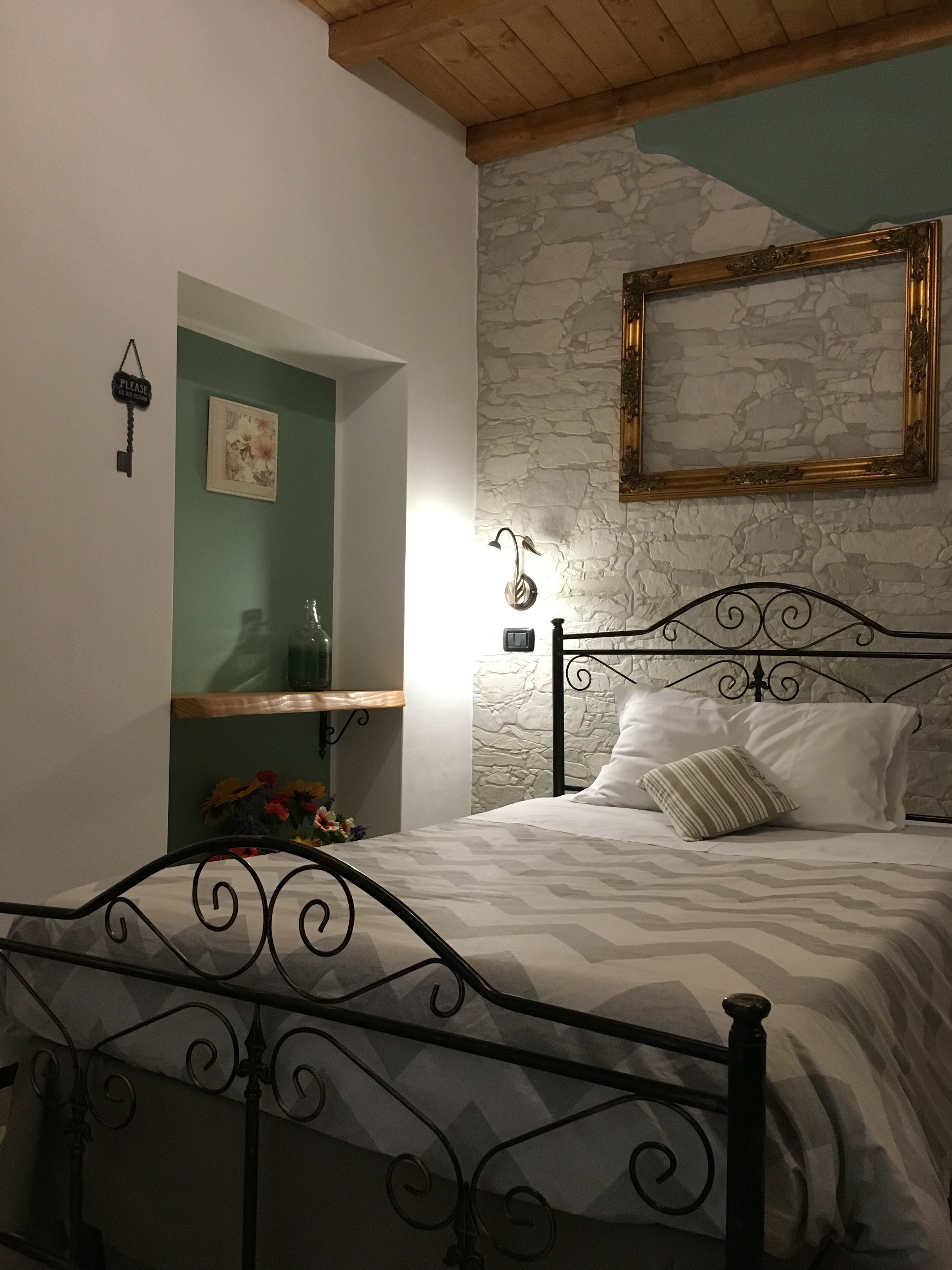 Un dormitorio con cama, pared de piedra, techo de madera y un cuadro enmarcado en la pared.