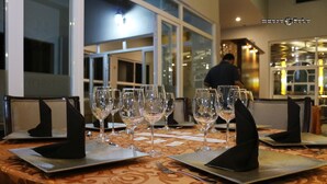 Una mesa de comedor dispuesta con varias copas de vino y cubiertos, con un mantel estampado y una persona al fondo.