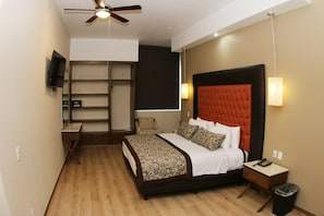 Una habitación de hotel moderna con una cama grande, un escritorio, una silla, un televisor y un ventilador de techo.