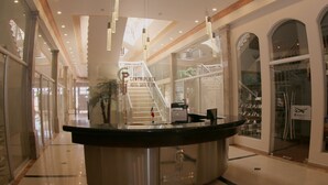 Zona de recepción de hotel con un mostrador curvo, una escalera que sube a un nivel superior y vista del vestíbulo.