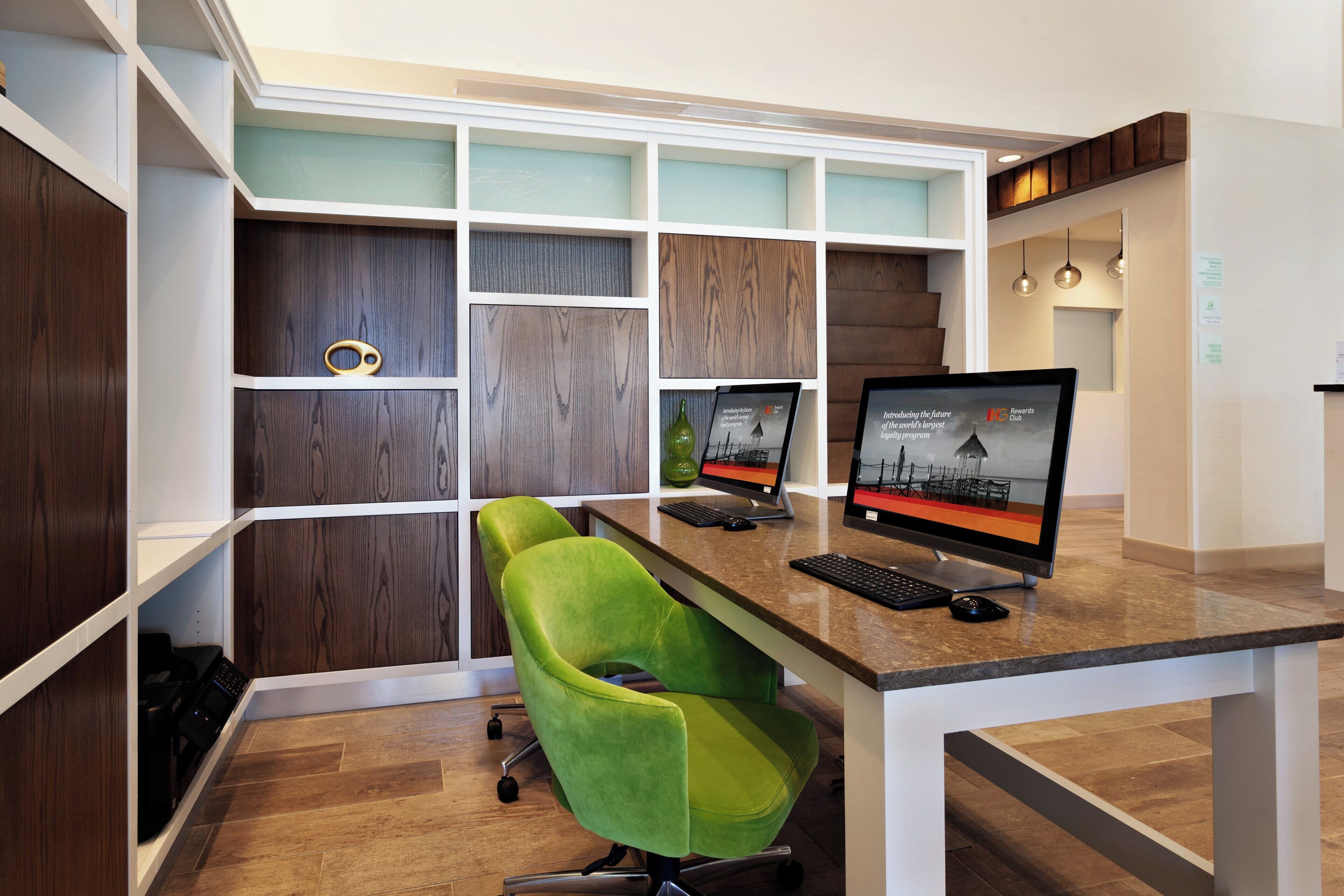 A modern office space with a desk, two monitors, a green chair, and a built-in shelving unit.