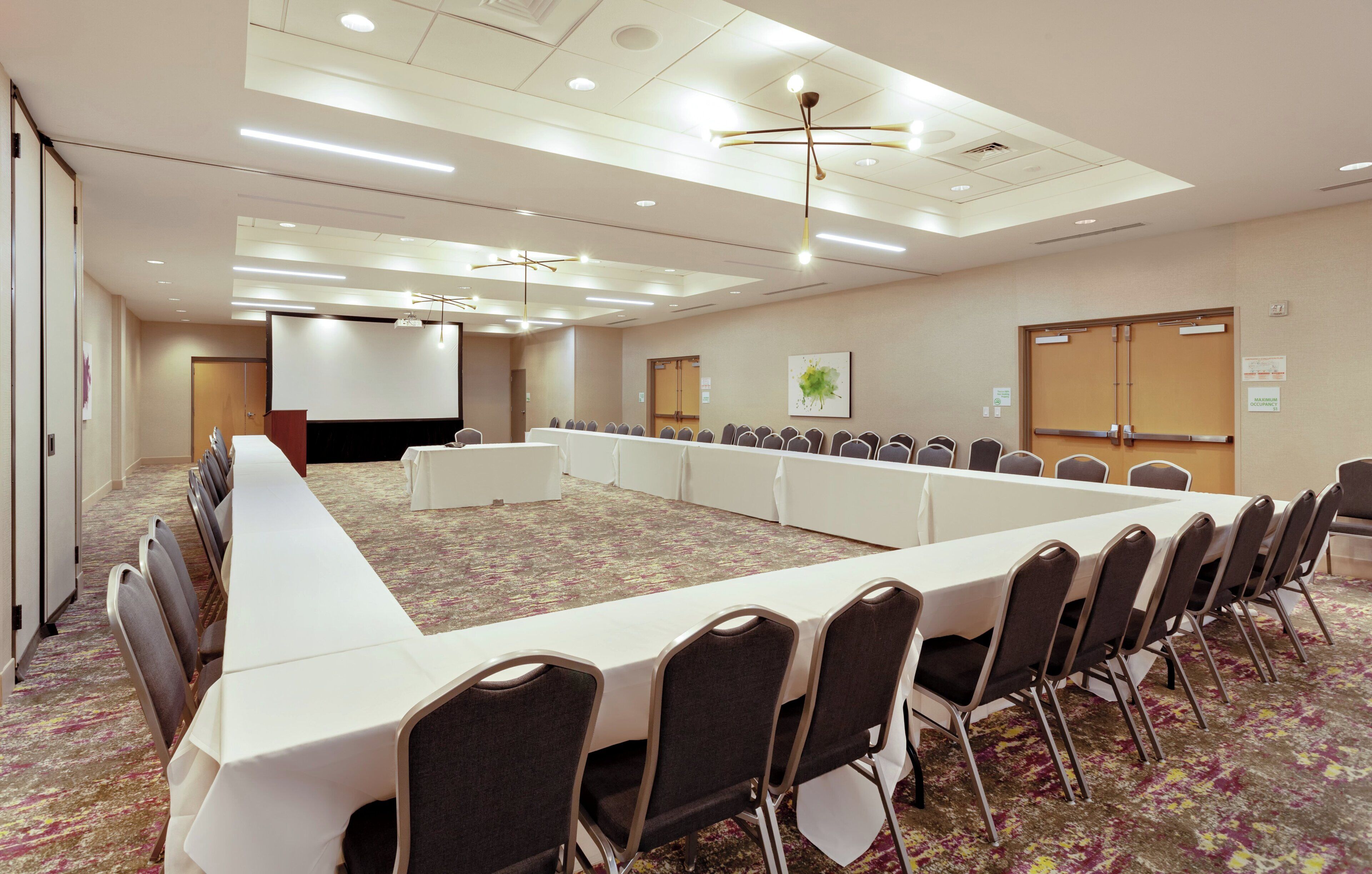 A conference room with a long table, chairs, a projector screen, and a carpeted floor.