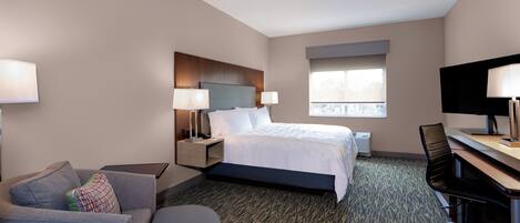 Ein Hotelzimmer mit Bett, Schreibtisch, Sessel, Sofa und Fernseher.