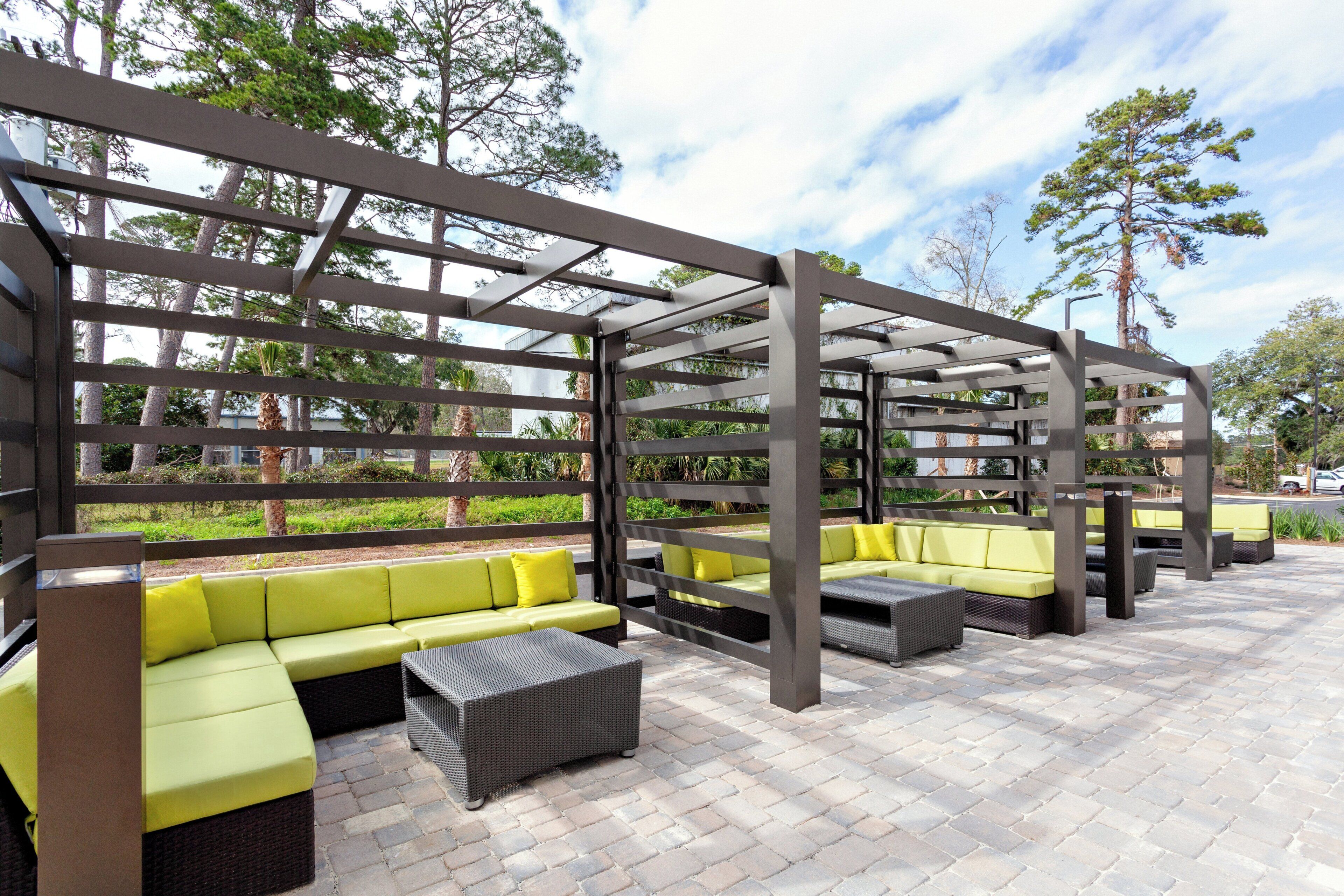 Een terras met meerdere banken en stoelen, een pergola en een geplaveid terras.