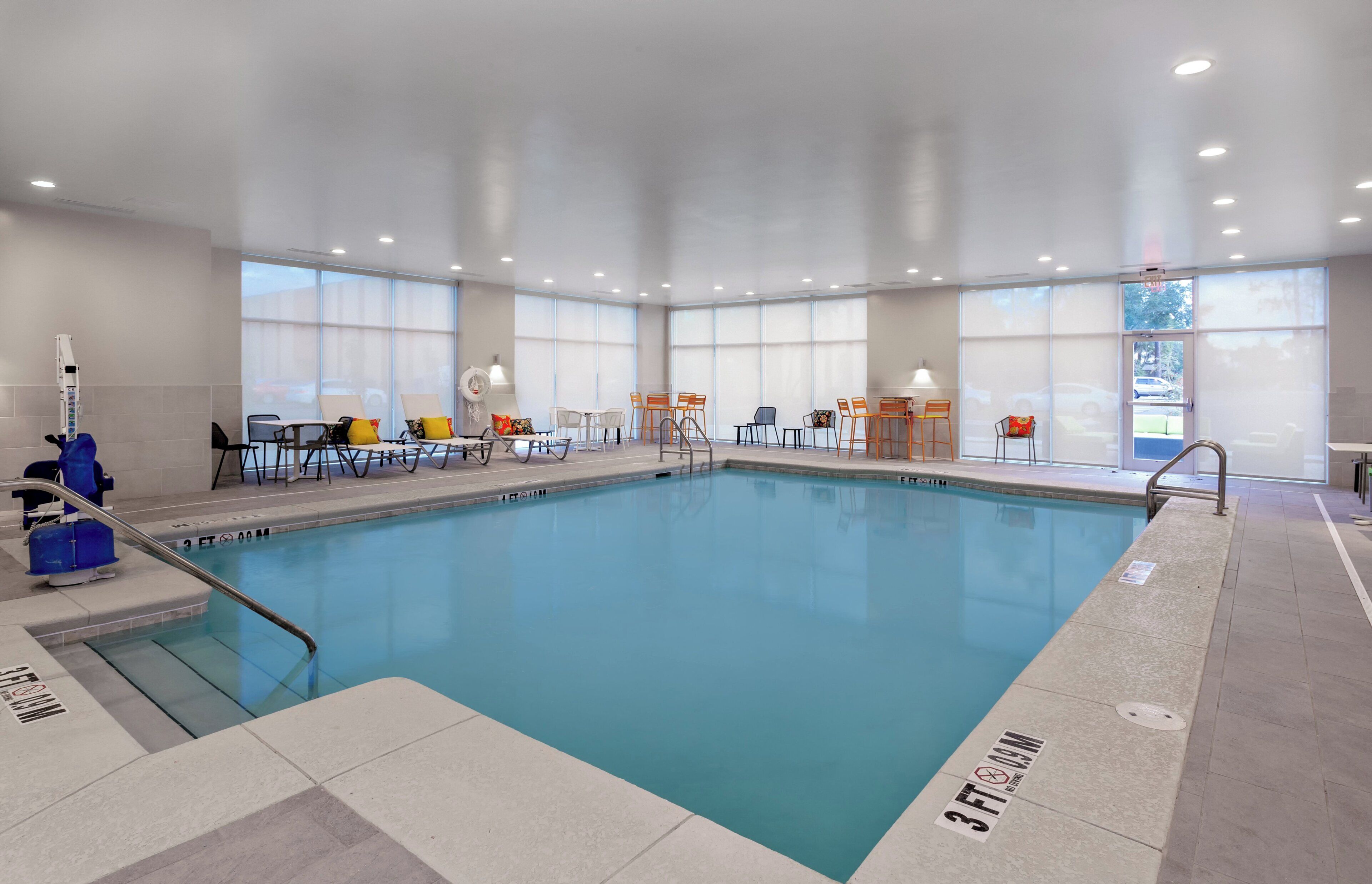 A large indoor swimming pool with multiple seating areas and a clear view of the outside through large windows.