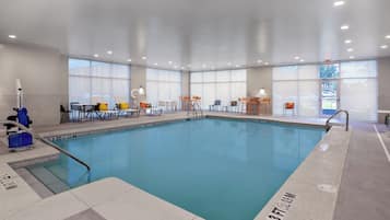 A large indoor swimming pool with multiple seating areas and a clear view of the outside through large windows.