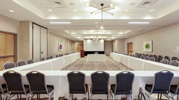 A conference room with a long table, rows of chairs, and a modern chandelier.