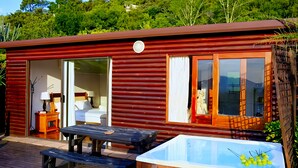 Uma cabana de madeira com porta de vidro deslizante, uma banheira de hidromassagem e uma mesa de piquenique do lado de fora.