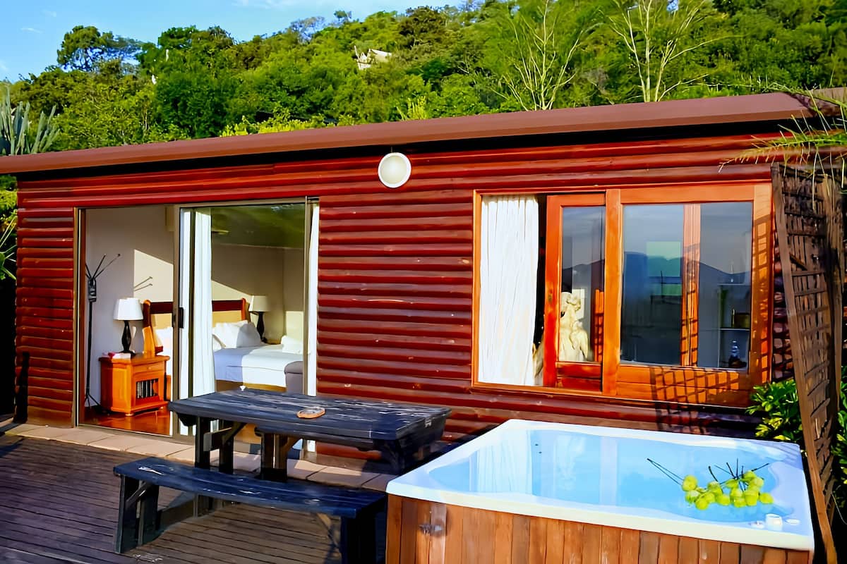 Eine Holzhütte mit Schiebetür, Whirlpool und Picknicktisch außen.