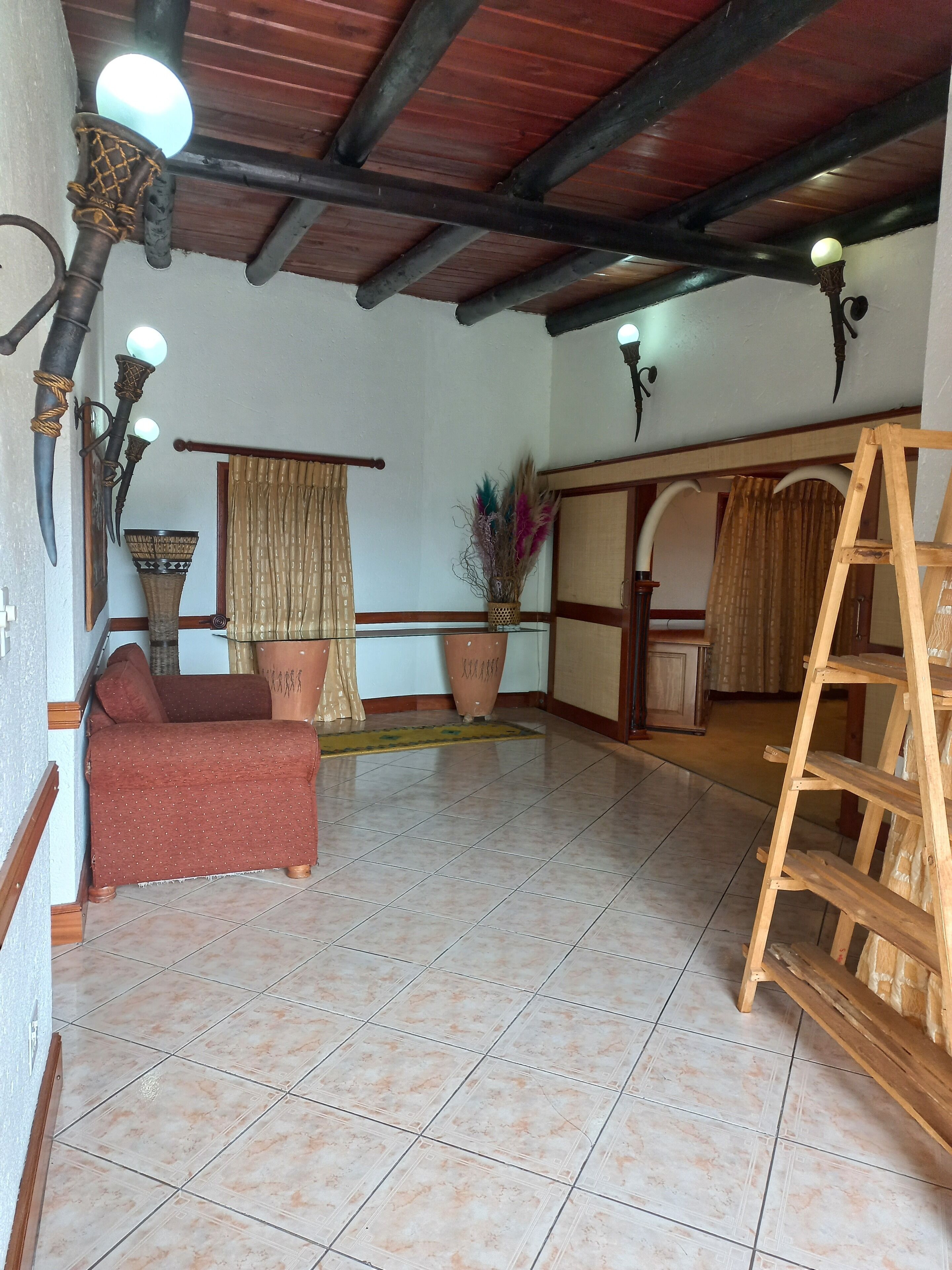 Une pièce avec un sol carrelé, un canapé en bois, une échelle, une plante en pot et un élément décoratif fixé au mur.