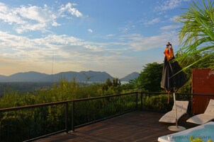 Una terraza de madera con sillones de descanso y una sombrilla, con vistas a un paisaje montañoso.