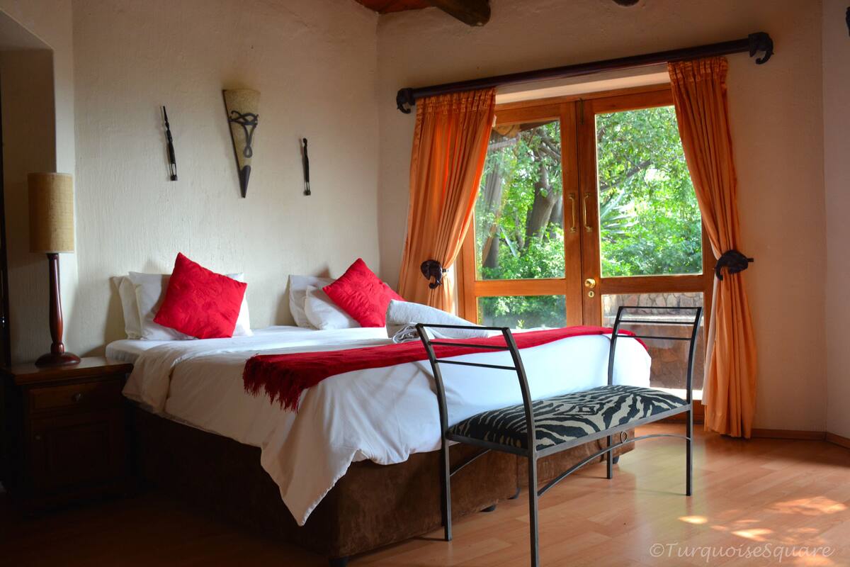 Ein Schlafzimmer mit einem Bett, einem Sessel, einem Nachttisch und einem Fenster mit Vorhängen.
