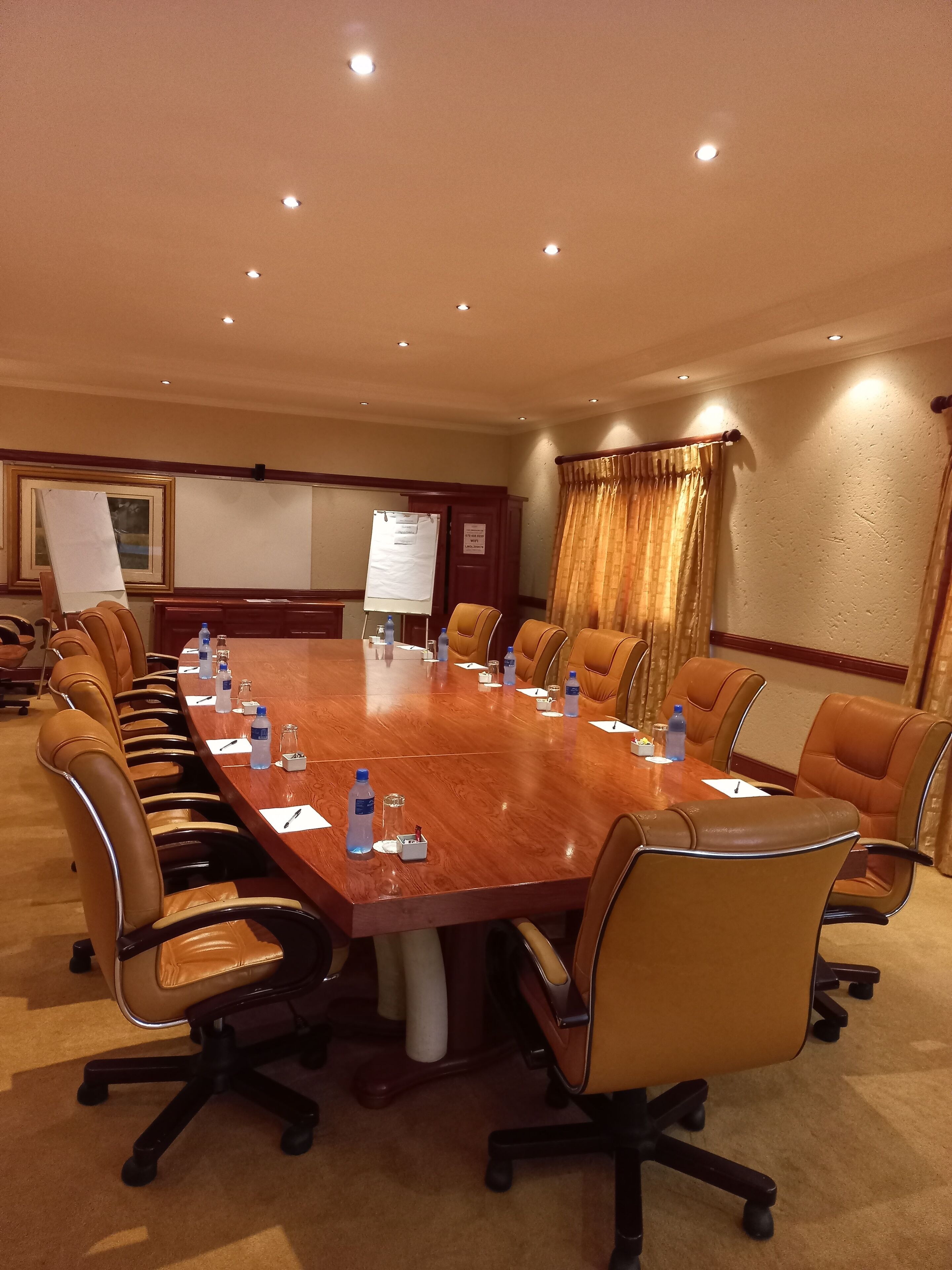 A conference room with a long wooden table, brown leather chairs, water bottles, and a whiteboard.