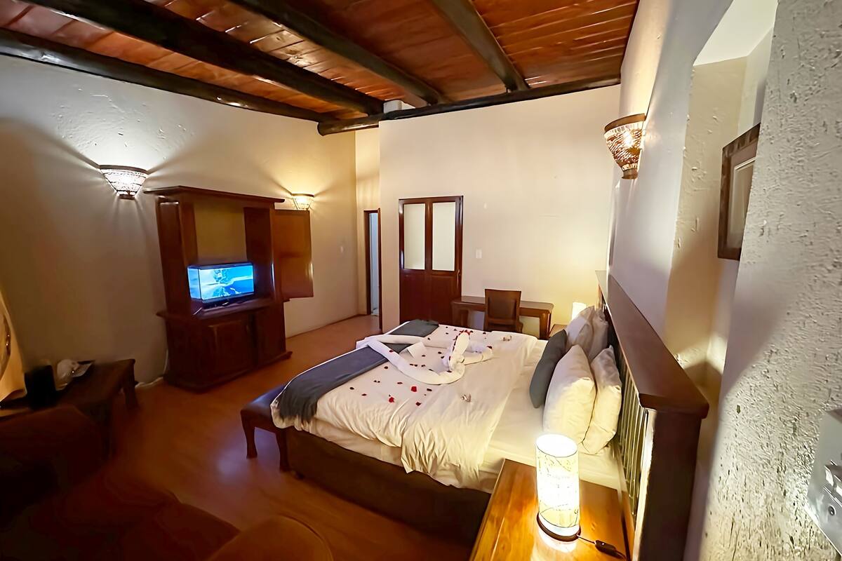 Ein gemütliches Schlafzimmer mit Bett, Nachttisch, Lampe, Fernseher und einem Holztisch.