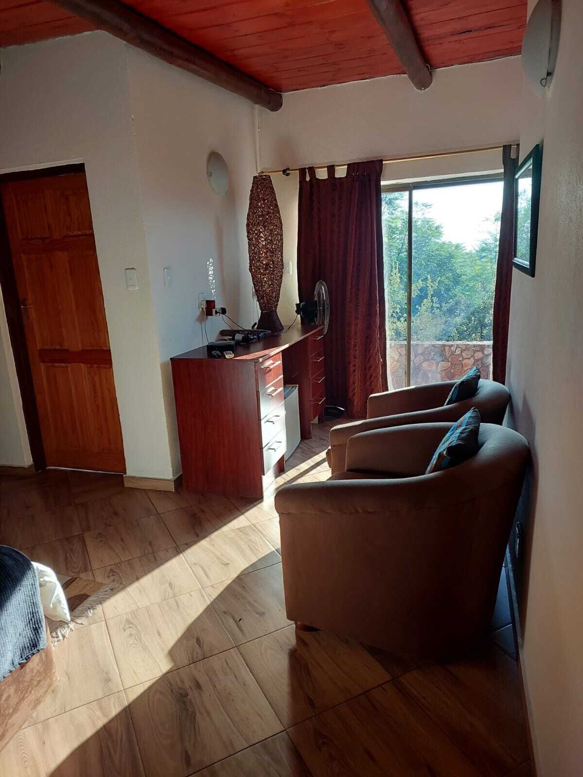 A living room with a wooden floor, a sofa set, a wooden cabinet, and a large window with curtains.