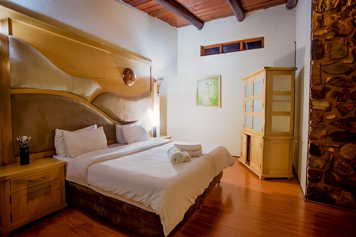 Ein Schlafzimmer mit hölzernem Kopfteil, einem Bett mit weißer Bettwäsche, einem Nachttisch, einem Holzschrank und einer Steinsäule.