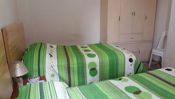 Un dormitorio con dos camas, un armario de madera y una silla de plástico blanca.