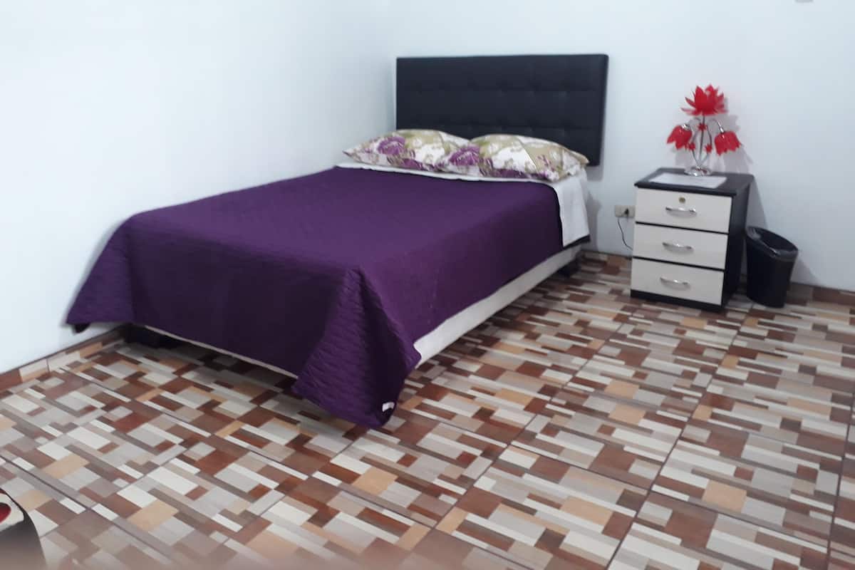 A bedroom with a bed, a nightstand, and a trash bin.