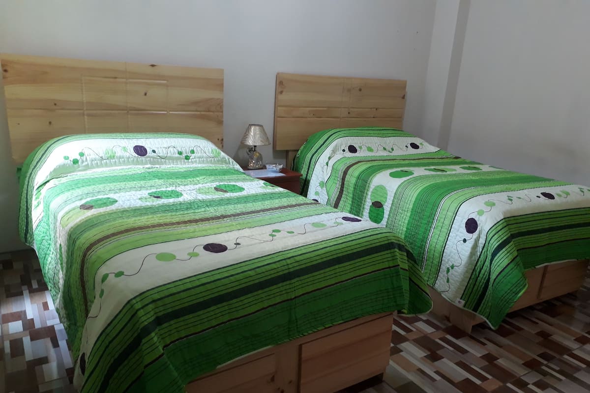A bedroom with two wooden beds, each with green and white bedding, a nightstand, and a lamp.