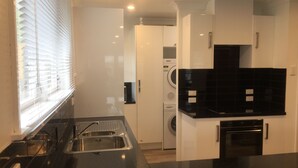 A modern kitchen with a stainless steel sink, black countertops, a built-in oven, and a washing machine in the background. - 3 & 4 Bedroom Houses in Seaview Crescent (Picton)
