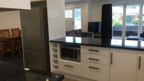 A modern kitchen with white cabinets, a black countertop, and a built-in microwave. There is a dining area with wooden chairs and a table. - 3 & 4 Bedroom Houses in Seaview Crescent (Picton)