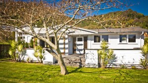 A white two-story house with a front porch, surrounded by a well-maintained lawn and several palm trees. - 3 & 4 Bedroom Houses in Seaview Crescent (Picton)