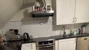 Una cuina moderna amb armaris blancs, un forn d'acer inoxidable, una cafetera i un rentaplats.