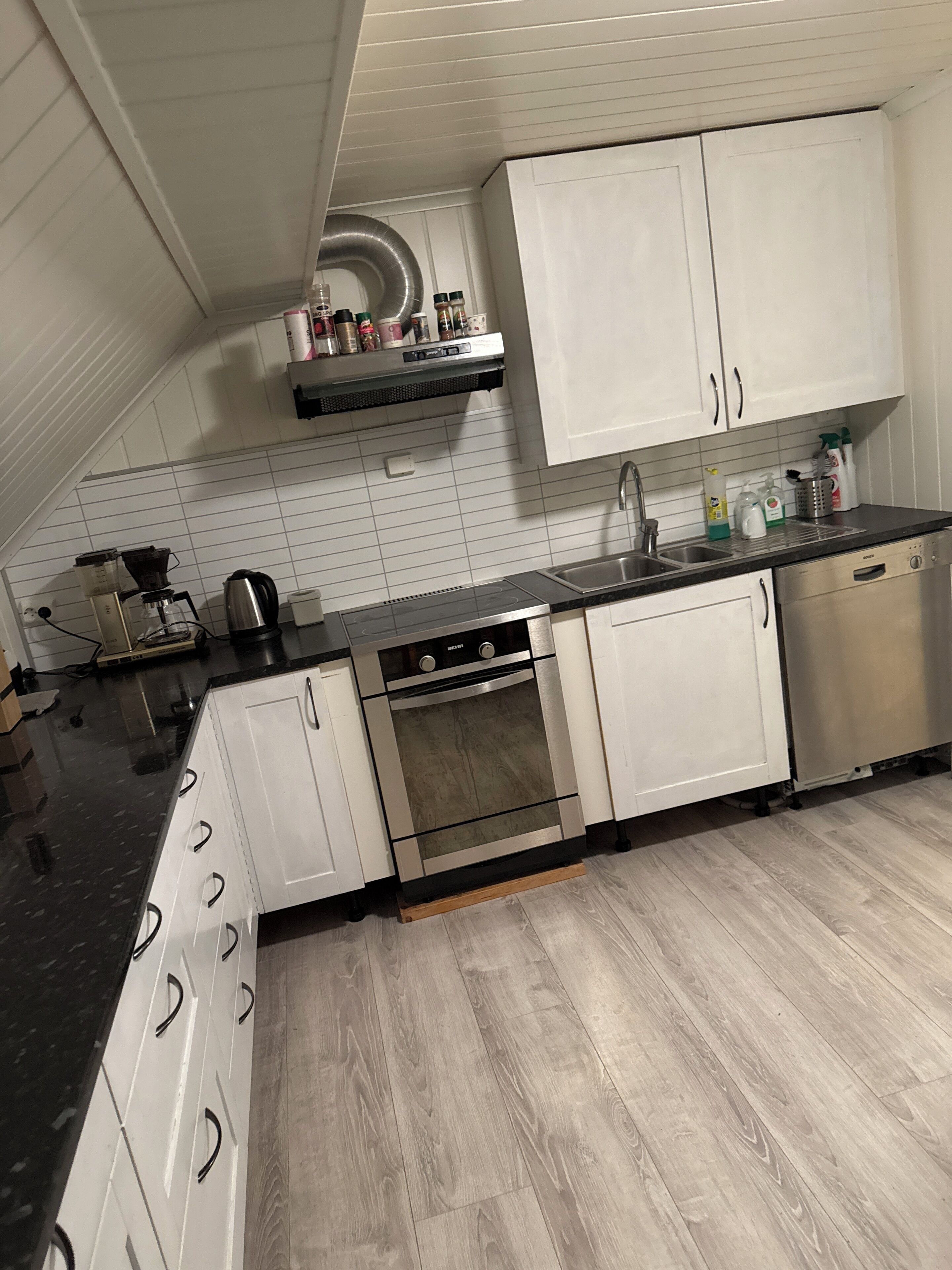 A modern kitchen with white cabinets, a black countertop, and a stainless steel oven.