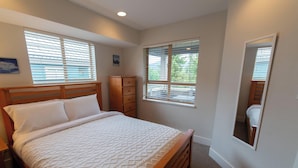 Un dormitorio con una cama, un tocador, dos ventanas con persianas y un espejo en la pared.