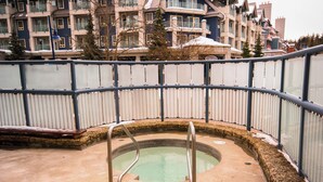 Un área de piscina con barandilla de vidrio curva, una piscina pequeña y un borde de piedra.