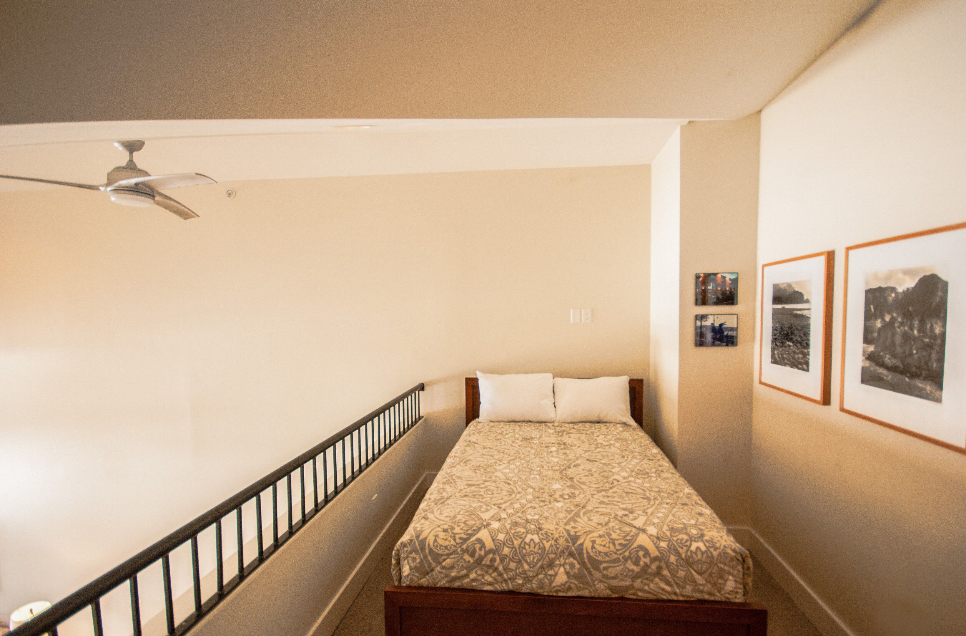 Un dormitorio con una cama, un ventilador de techo, una escalera y cuadros en la pared.