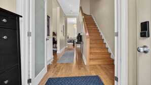 A hallway with a wooden staircase, a black cabinet, and a door with a sensor.