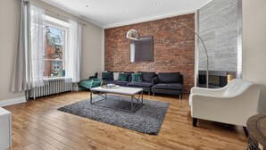 A modern living room with a brick wall, a fireplace, a white sofa, a white armchair, and a coffee table.