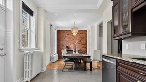 A modern kitchen with a brick wall, white cabinetry, and a dining area with a table and chairs. - Downtown Montreal Victorian Retreat | Indoor Parking, Walk Everywhere (Le Plateau-Mont-Royal)